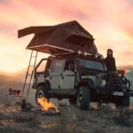 Ein Dachzelt auf einem Auto, geöffnet in einer malerischen Berglandschaft bei Sonnenuntergang.