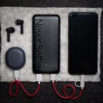 Eine schwarze Powerbank mit mehreren Kabeln liegt neben Gitarreneffektpedalen auf einer Holzbank.