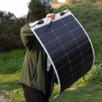 Faltbares Solarmodul ausgebreitet auf einem Campingtisch, daneben ein aufgeladenes Smartphone und eine Powerbank.