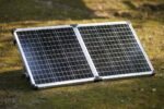 Faltbares 100W-Bifacial-Solarmodul auf einem Campingtisch, das von beiden Seiten Sonnenlicht einfängt und einen Powerbank-Akku lädt.