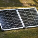 Faltbares 100W-Bifacial-Solarmodul auf einem Campingtisch, das von beiden Seiten Sonnenlicht einfängt und einen Powerbank-Akku lädt.