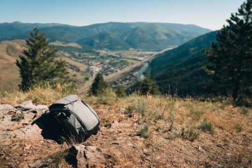 Peak Design Everyday Sling 3L V3 in Schwarz, um die Schulter getragen, mit geöffnetem Hauptfach und einem schnell erreichbaren Smartphone.